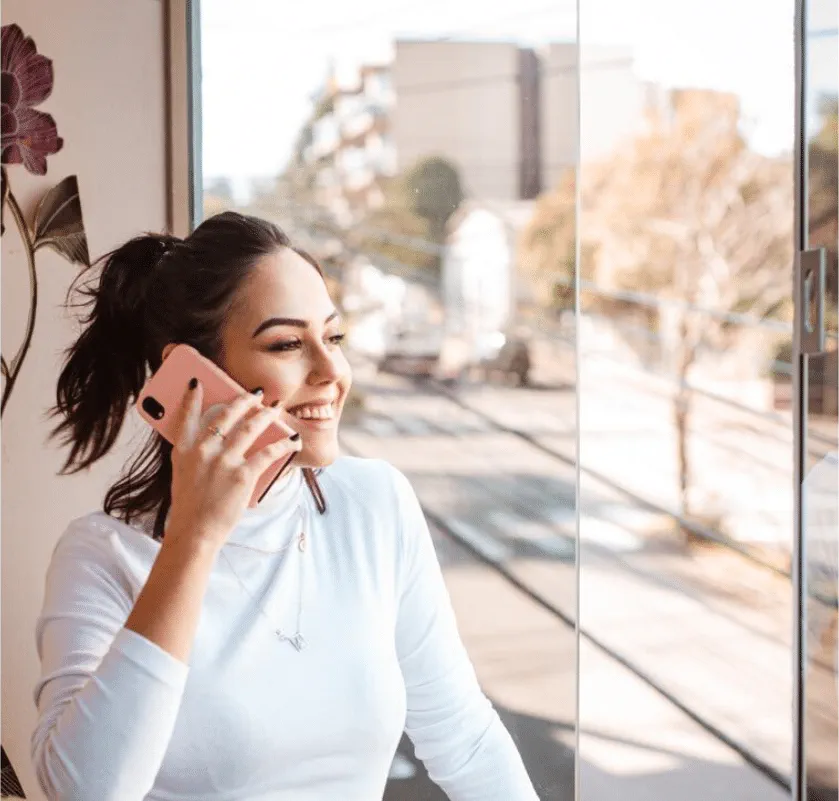 A stock photo of a woman talking on the phone; she is looking out of her office window.